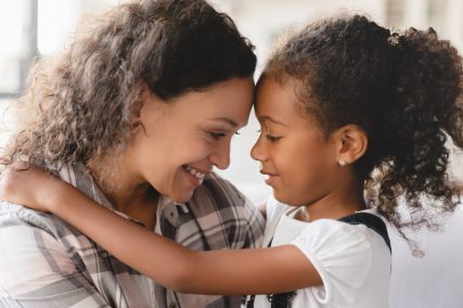 African-american mother and small little young preteen daughter hugging embracing with eyes closed sharing love and care. Motherhood. Happy Mother`s day!